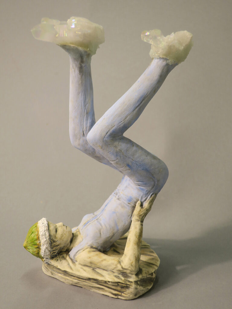 Painted terracotta sculpture by Jordan MacLachlan of an upside down cycling man with crystals for feet.
